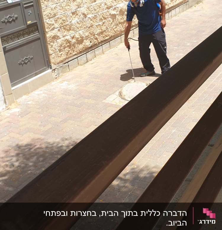 אדם עם מסכת מגן מרסס חומר הדברה על מדרכה